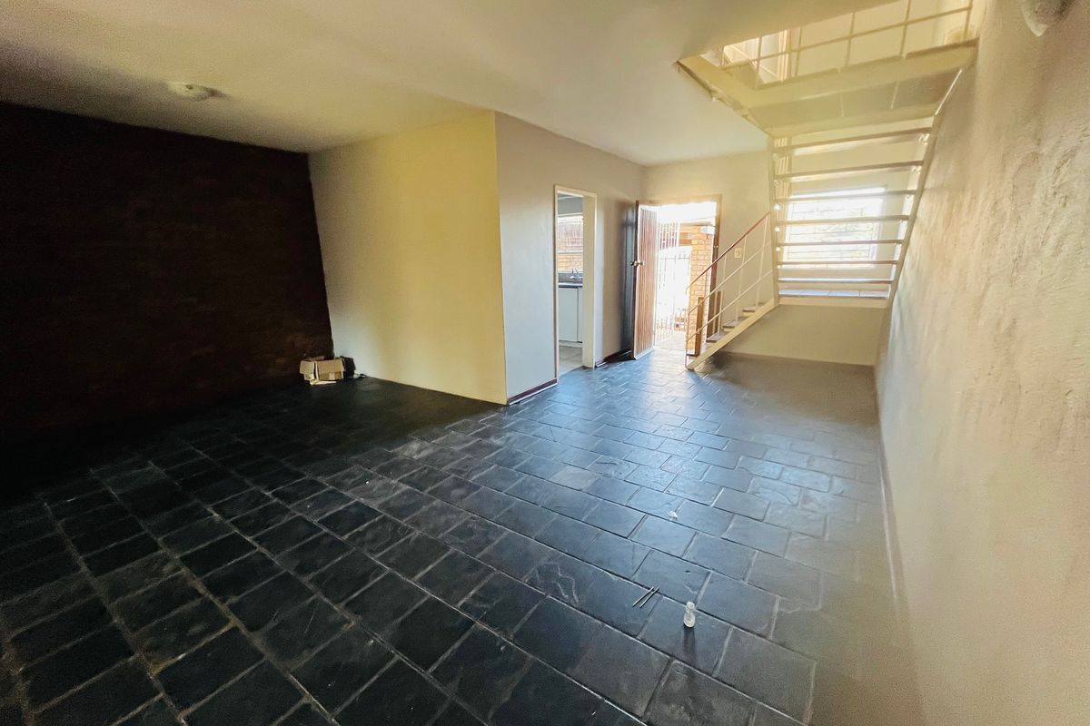 An open-plan living area featuring dark slate tile flooring, an exposed brick accent wall, and a metal staircase leading to the upper level.