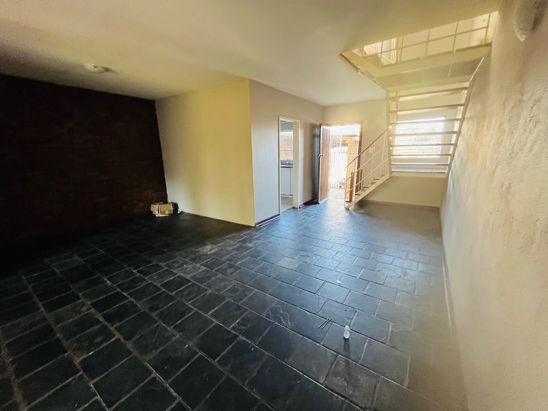An open-plan living area featuring dark slate tile flooring, an exposed brick accent wall, and a metal staircase leading to the upper level.