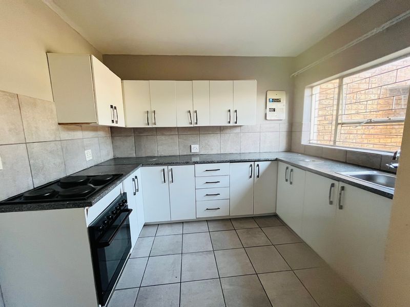 A functional kitchen featuring white built-in cabinetry, granite countertops, an electric stove, and tiled flooring with a window providing natural light.