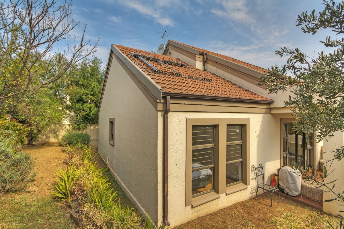 Rear view of the townhouse featuring terracotta roof tiles, integrated solar water heating panels, and aluminium window frames overlooking a private garden area.
