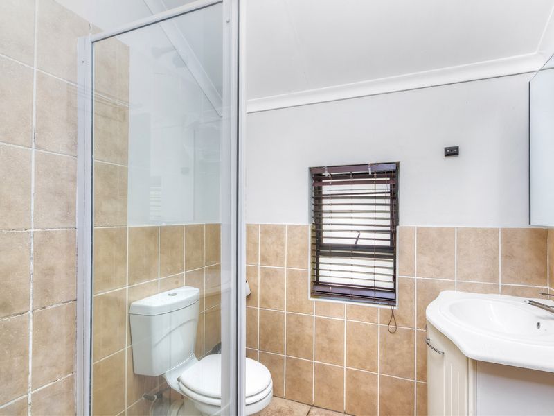 A functional bathroom featuring a shower enclosure, toilet, and vanity basin with neutral wall tiling.