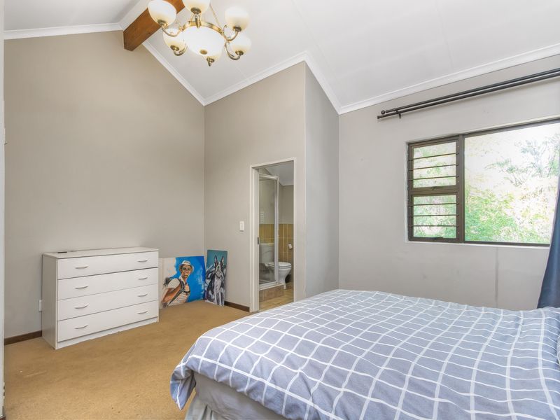 Spacious bedroom featuring a vaulted ceiling with an exposed timber beam, carpeted flooring, and an attached en-suite bathroom.