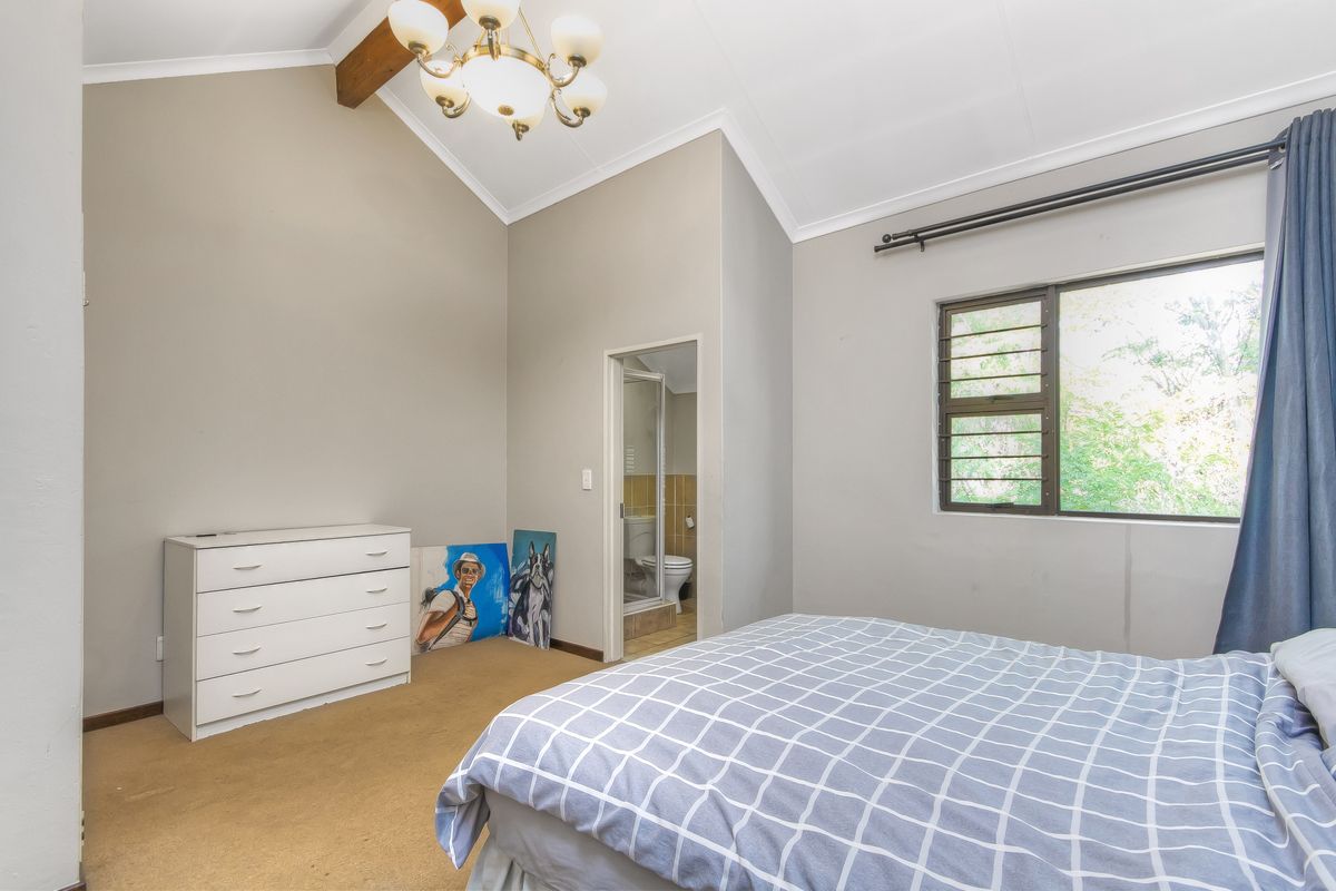 Spacious bedroom featuring a vaulted ceiling with an exposed timber beam, carpeted flooring, and an attached en-suite bathroom.