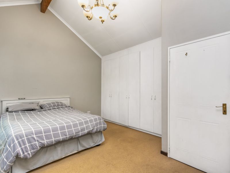 A bedroom featuring a vaulted ceiling with an exposed timber beam, extensive built-in cupboard storage, and neutral wall finishes.