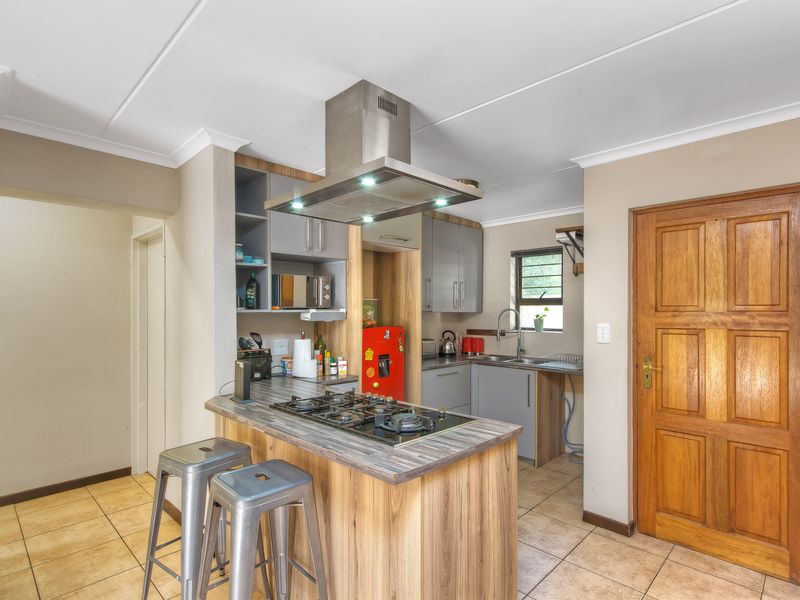 Compact kitchen featuring a central island with a gas hob, stainless steel extractor fan, built-in cabinetry, and tiled flooring.