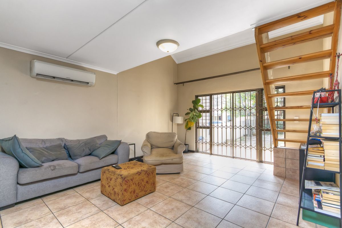 A living room featuring tiled flooring, a wooden staircase, and a split-system air conditioner, with direct access to the exterior through a security gate.