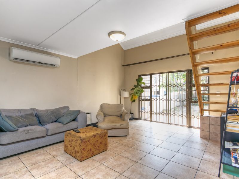 A living room featuring tiled flooring, a wooden staircase, and a split-system air conditioner, with direct access to the exterior through a security gate.