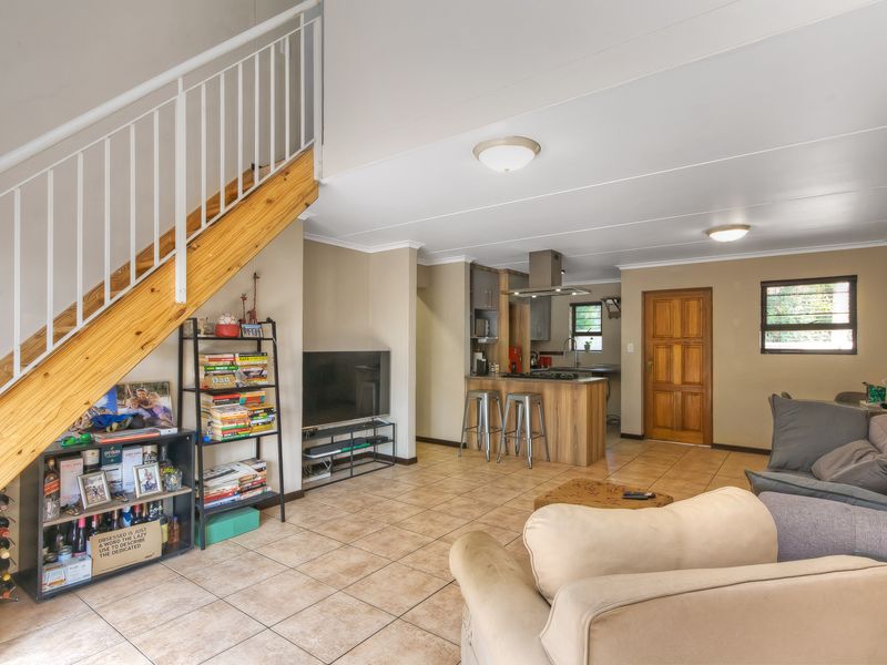 Open-plan living area featuring tiled floors, a staircase with metal balustrades, and a functional kitchen with built-in cabinetry and a central island.