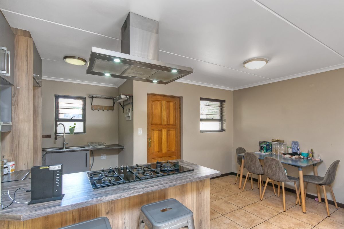 A functional kitchen featuring a central island with a gas hob, stainless steel extractor fan, ample cabinetry, and tiled flooring.