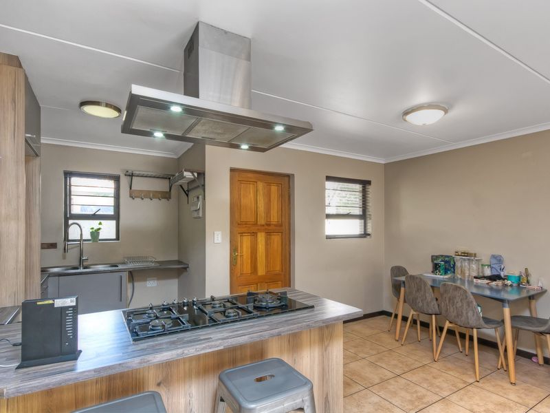 A functional kitchen featuring a central island with a gas hob, stainless steel extractor fan, ample cabinetry, and tiled flooring.
