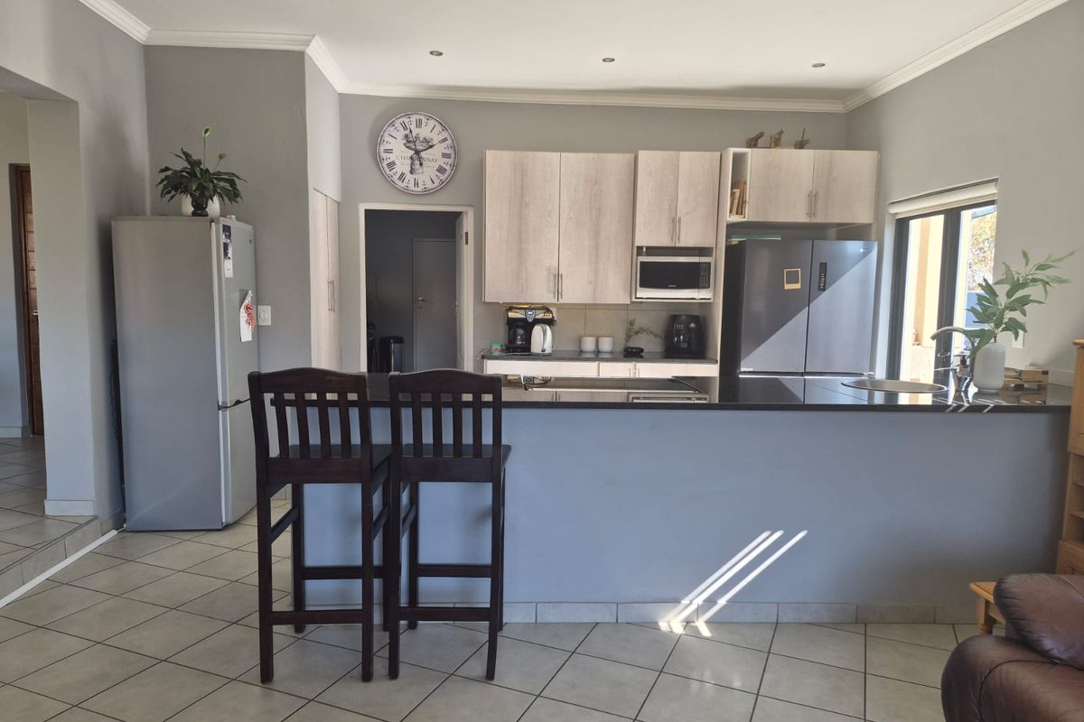 A functional kitchen featuring light wood cabinetry, a dark granite breakfast bar island, tiled flooring, and recessed lighting.
