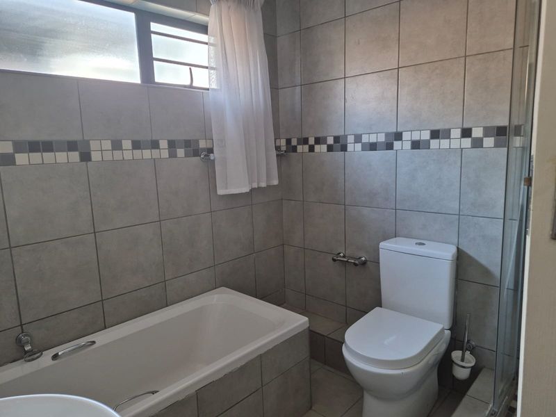 A functional bathroom featuring a bathtub, toilet, and shower enclosure with neutral grey wall and floor tiling.