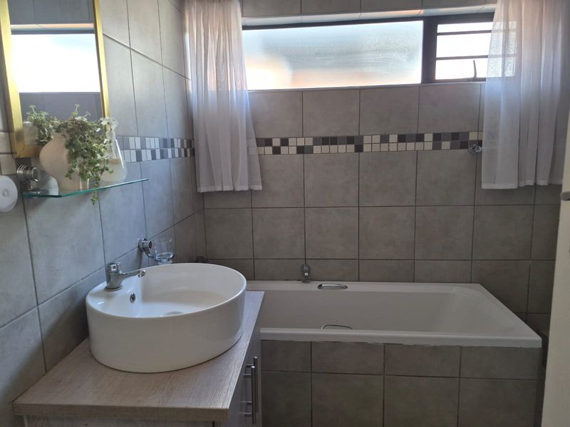 A well-maintained bathroom featuring a modern vessel sink on a vanity cabinet, a bathtub, and neutral wall tiling.