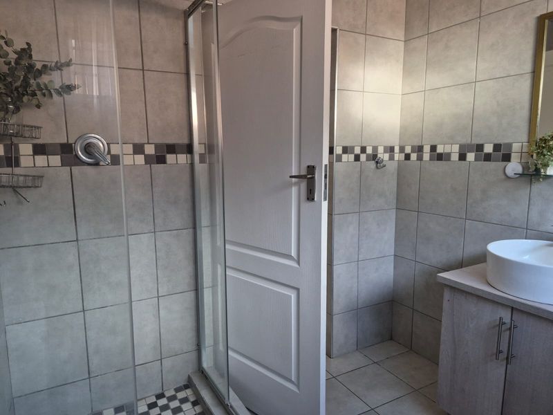 A functional bathroom featuring a glass shower enclosure, tiled wall finishes, and a modern vessel sink set on a vanity cabinet.