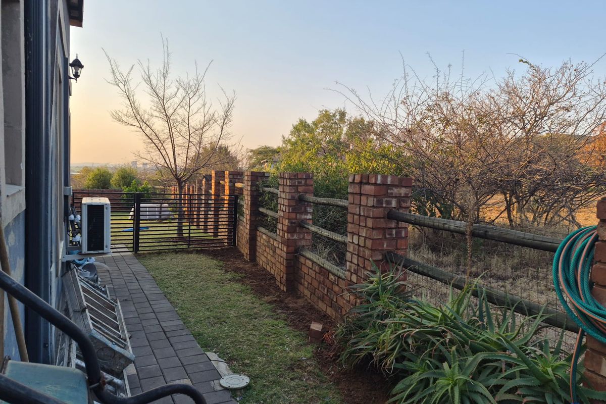 A rear garden area featuring a paved walkway, brick and timber boundary fencing, and an external air conditioning unit.