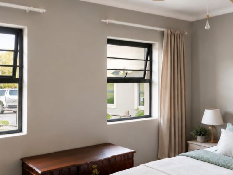 A well-maintained bedroom featuring neutral wall tones, black-framed casement windows, and a ceiling fan, offering a bright and comfortable living space.
