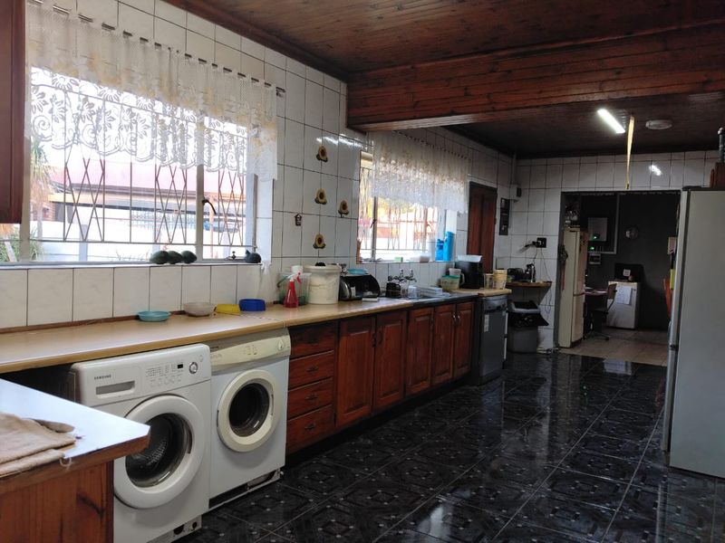 A functional kitchen featuring wooden cabinetry, laminate countertops, tiled backsplash, and dark floor tiles, with an adjacent utility area and timber ceiling.