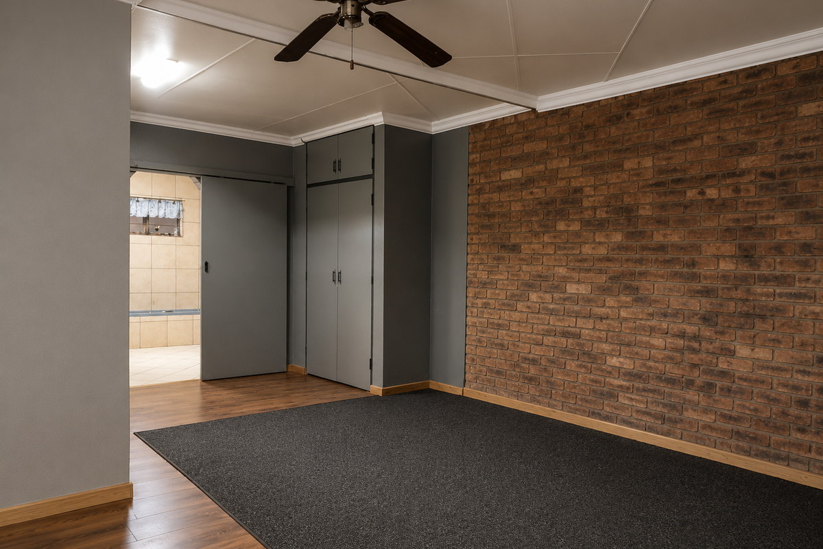 Spacious bedroom featuring a striking exposed brick wall, built-in cupboards, a ceiling fan, and a sliding door leading to an adjoining bathroom.