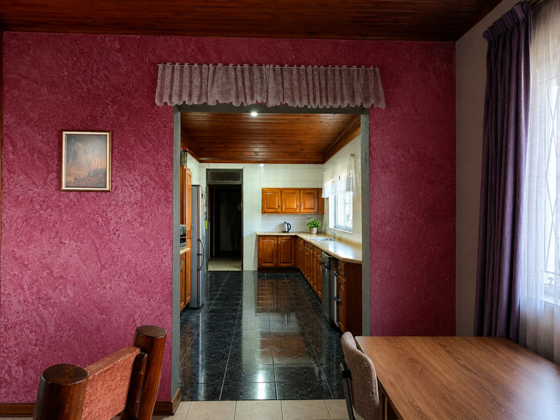 A functional kitchen featuring wooden cabinetry, tiled flooring, and a tiled backsplash, connected to an adjacent living area with a distinct textured wall finish.
