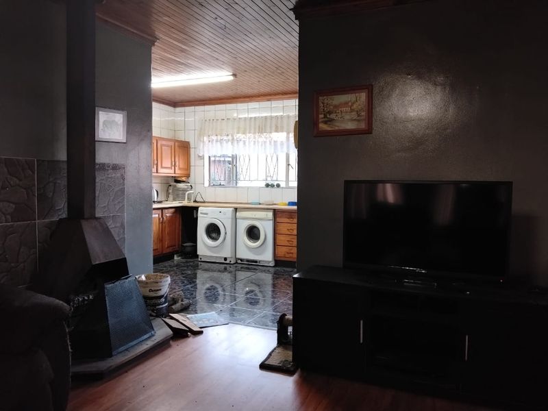 Open plan living area featuring a freestanding fireplace, wooden ceiling, and an adjoining kitchen area with built-in cabinetry and laundry appliance connections.