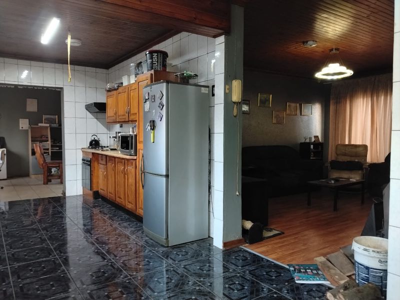 Open-plan kitchen and living area featuring timber ceilings, tiled kitchen flooring, and built-in wooden cabinetry with integrated appliances.