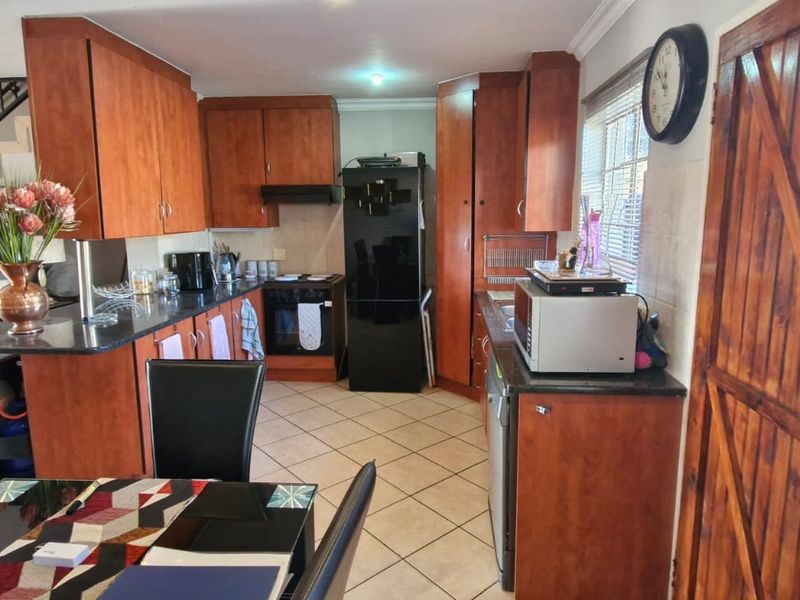 Open-plan kitchen featuring wooden cabinetry, stone countertops, and built-in appliances, seamlessly connected to the living and dining area with tiled flooring.