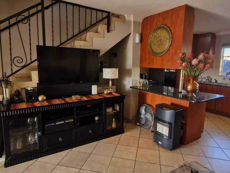 Open-plan living area featuring tiled floors, a staircase with wrought iron railing, and a kitchen with granite countertops and wooden cabinetry.