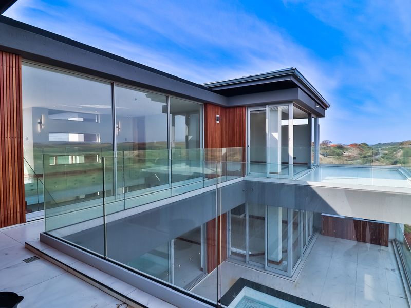 Modern multi-level balcony featuring glass balustrades, timber cladding, and large sliding doors, offering expansive views and seamless indoor-outdoor flow.