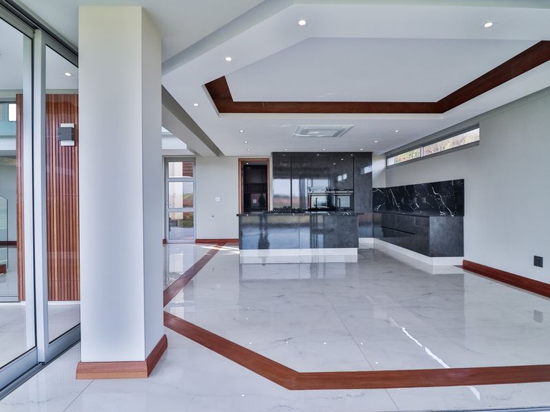 Spacious open-plan kitchen and living area featuring high-end marble-look flooring, modern cabinetry, built-in appliances, and expansive sliding glass doors.