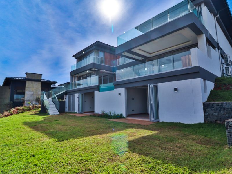 Modern multi-level residence featuring expansive glass balconies, bi-fold doors opening to the garden, and contemporary architectural finishes.