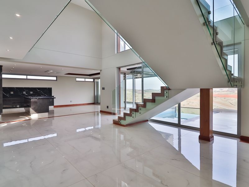 Spacious open-plan living area featuring high ceilings, polished marble-look flooring, and a striking floating staircase with glass balustrades, leading to outdoor views.