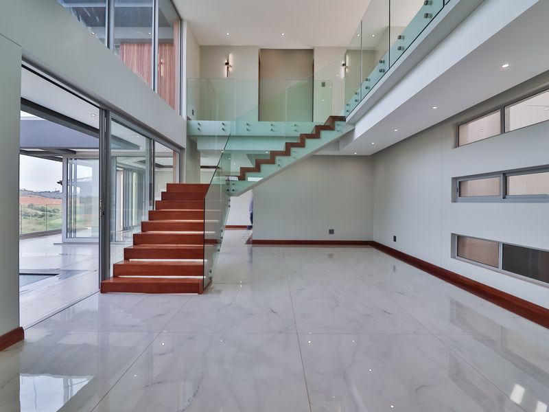 Spacious open-plan living area featuring a modern timber staircase with glass balustrades, polished marble flooring, and large sliding doors leading to the exterior.
