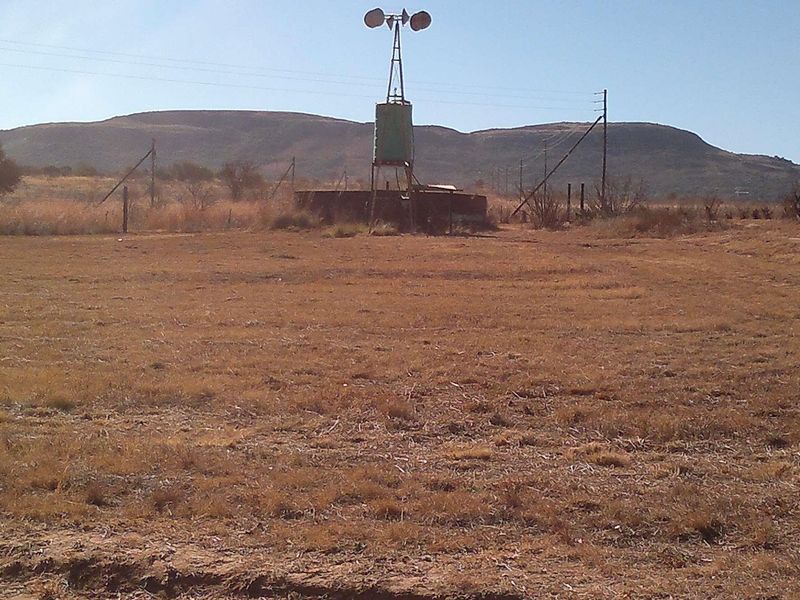 Open farm landscape featuring a traditional windmill, water tank, and reservoir set against a backdrop of rolling hills.