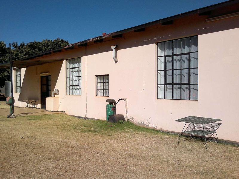 Rear elevation of a farm dwelling featuring steel-framed windows, a covered patio area, and exterior wall finishes requiring maintenance.