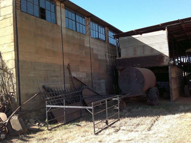 Exterior view of a farm outbuilding featuring masonry block walls, steel-framed windows, and an attached open-sided corrugated iron shed structure.