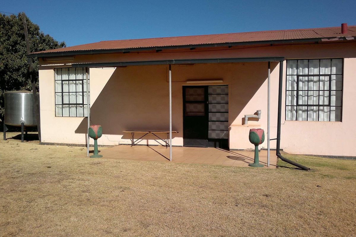 Rear view of a farm dwelling featuring a covered patio, steel-framed windows, and an external water tank on a dry lawn.