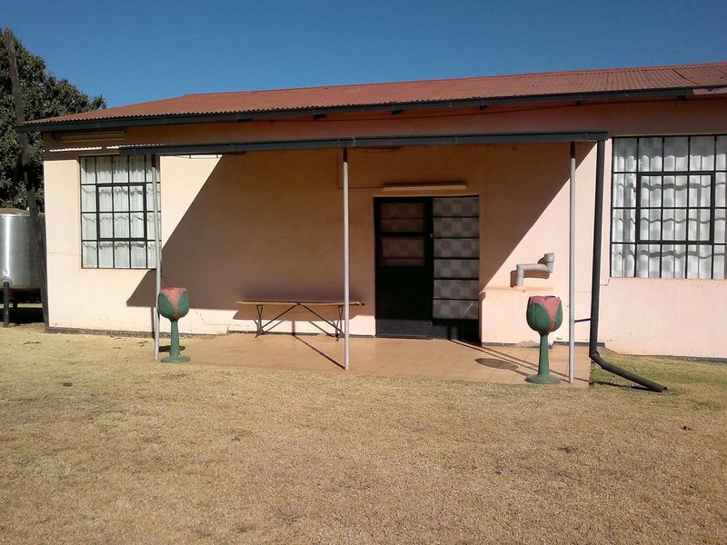 Rear view of a farm dwelling featuring a covered patio, steel-framed windows, and an external water tank on a dry lawn.