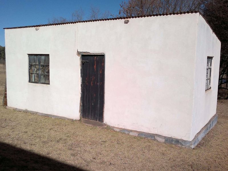 A small, detached outbuilding on a farm property featuring plastered masonry walls, a corrugated metal roof, and steel-framed windows.