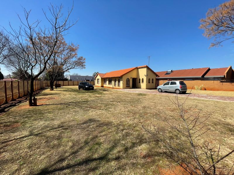 A spacious front yard with a paved driveway leading to a single-story house featuring a tiled roof and perimeter fencing.