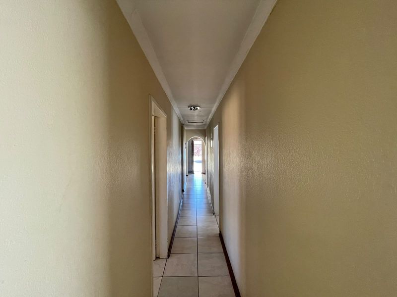 A long, empty residential hallway featuring neutral wall paint, tiled flooring, and simple ceiling lighting, providing access to various rooms within the home.