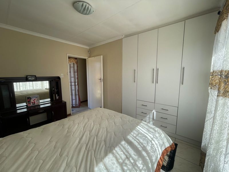 A bedroom featuring built-in cupboards, tiled flooring, and a ceiling light fixture, providing a functional and neutral living space.