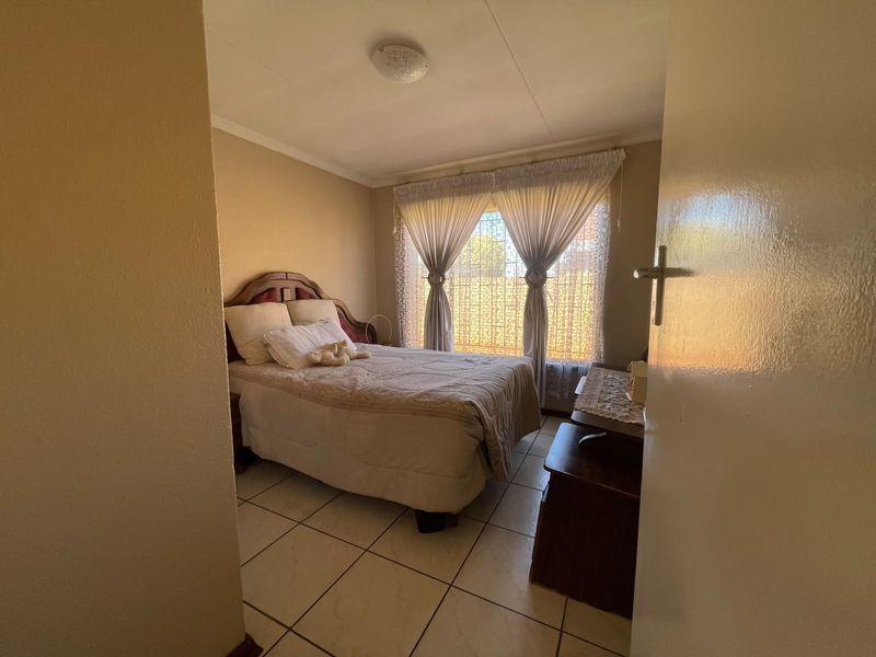 A functional bedroom featuring tiled flooring and a window fitted with security bars, providing natural light and a secure environment.