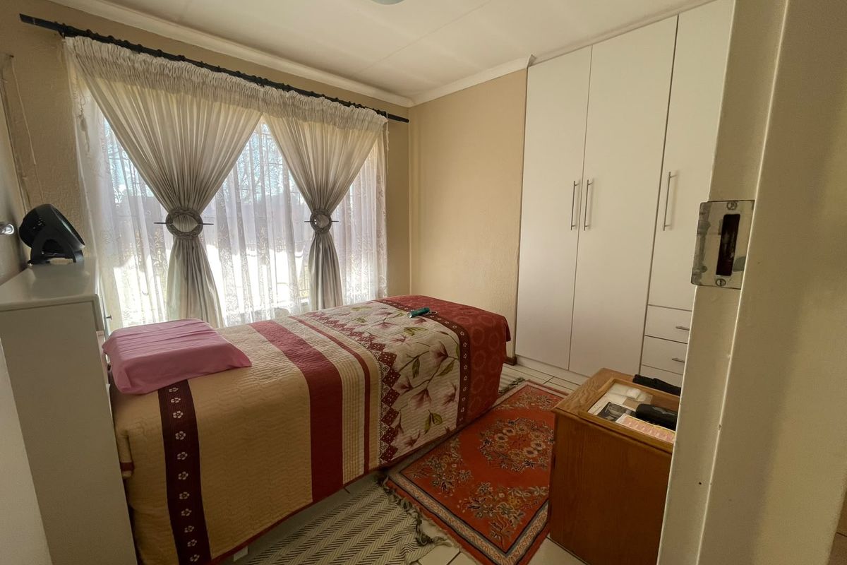 A functional bedroom featuring tiled flooring and a white built-in wardrobe, providing ample storage space.