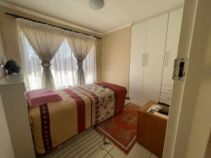 A functional bedroom featuring tiled flooring and a white built-in wardrobe, providing ample storage space.