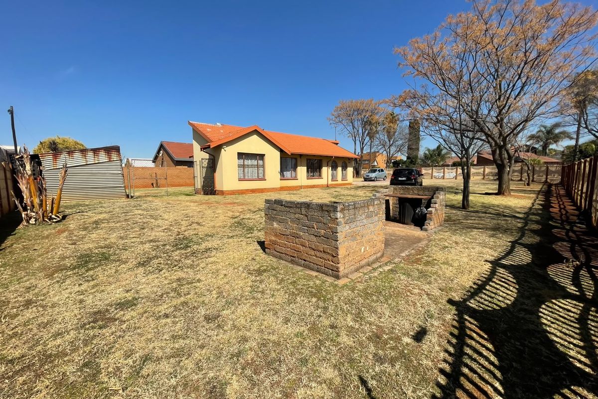 Spacious rear garden featuring a built-in brick braai area, tiled roof dwelling, and perimeter fencing.