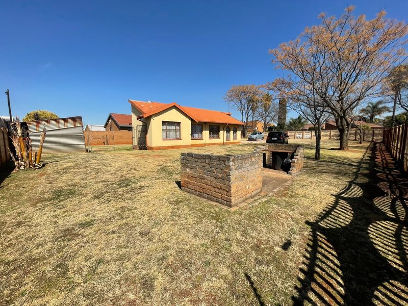 Spacious rear garden featuring a built-in brick braai area, tiled roof dwelling, and perimeter fencing.