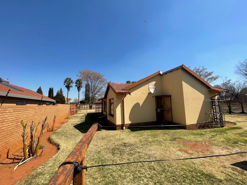 Rear view of the property featuring a brick boundary wall, tiled roof, and a private garden area with a security gate.