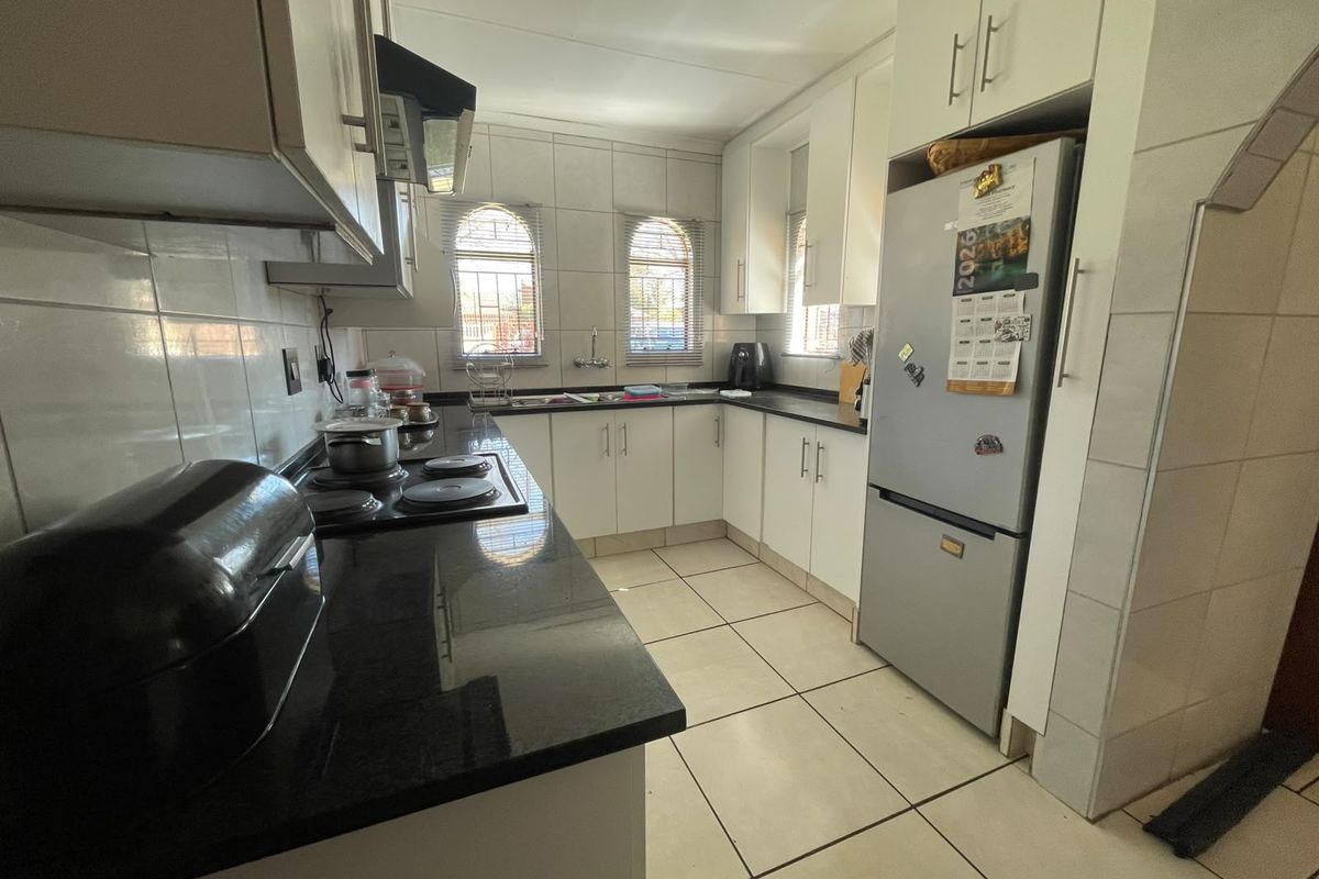 A functional kitchen featuring granite countertops, white cabinetry, tiled backsplash, and an electric hob with an extractor fan.