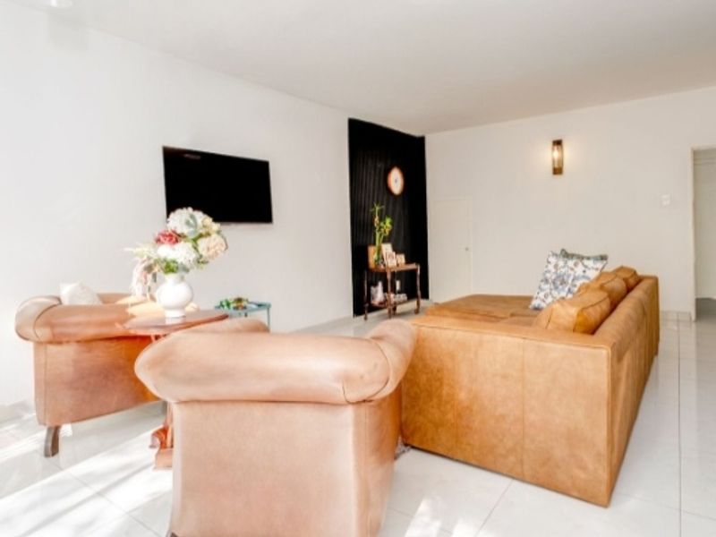 A bright living room featuring large format floor tiles, a dark accent wall, and wall-mounted lighting fixtures.