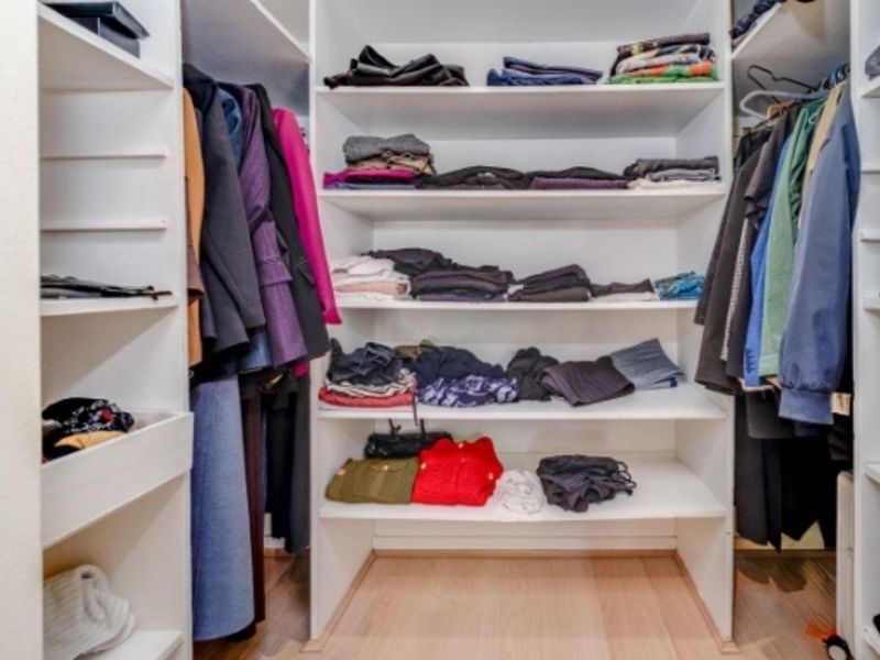A walk-in closet featuring extensive built-in shelving and hanging rails, providing ample storage space with light-toned laminate flooring.